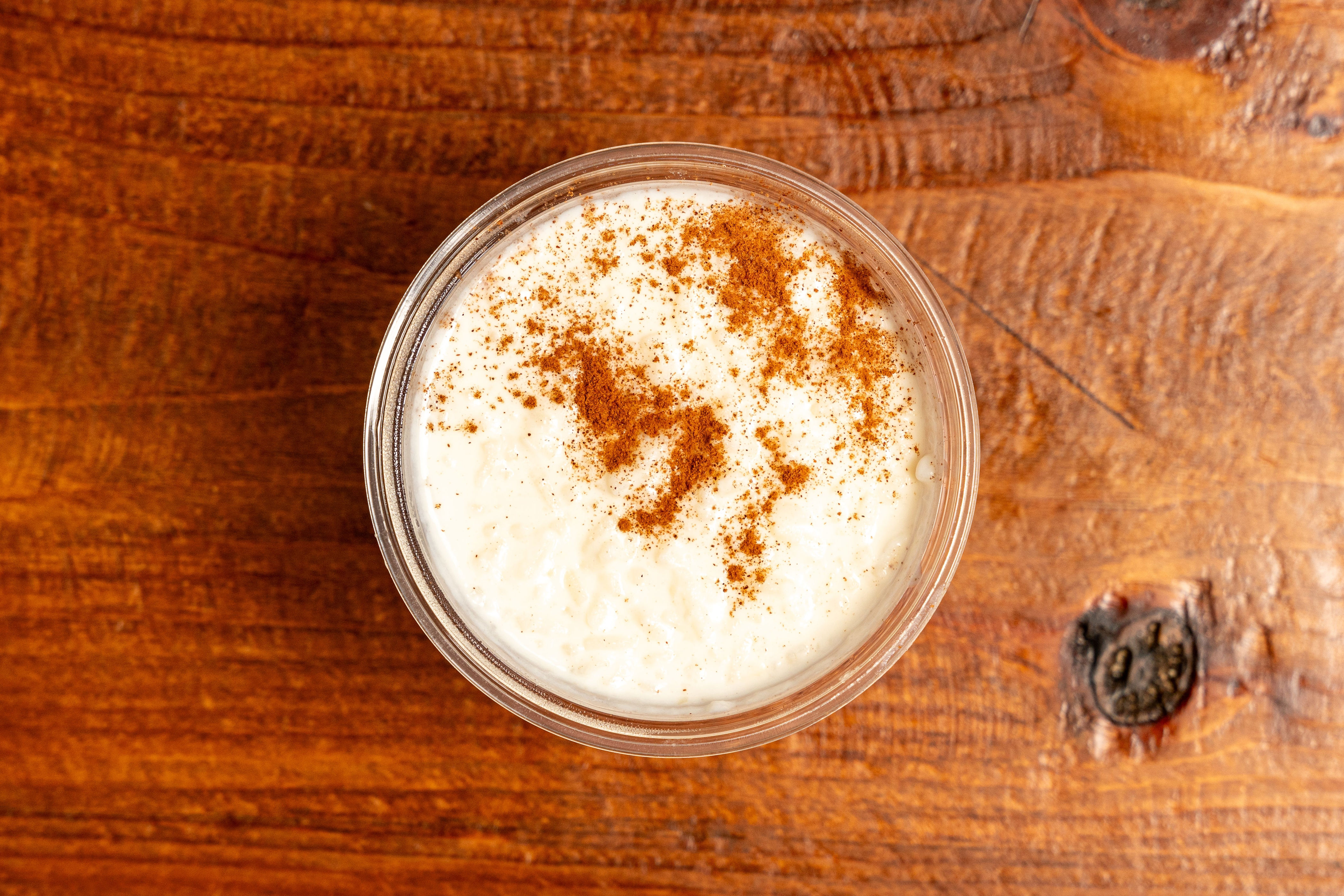 A glass of creamy rice pudding topped with a dusting of cinnamon on a wooden table