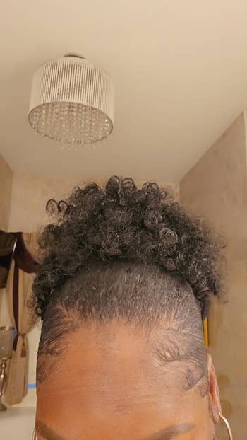 Person's hair styled in a curly updo with defined edges visible, set in an indoor setting with an elegant chandelier overhead