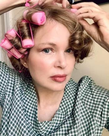 Person styling hair with rollers, wearing a gingham-patterned top