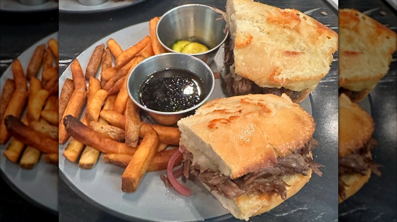 Braised Beef Sandwich with sides of au jus and pickle and French fries from Fernbank Public House