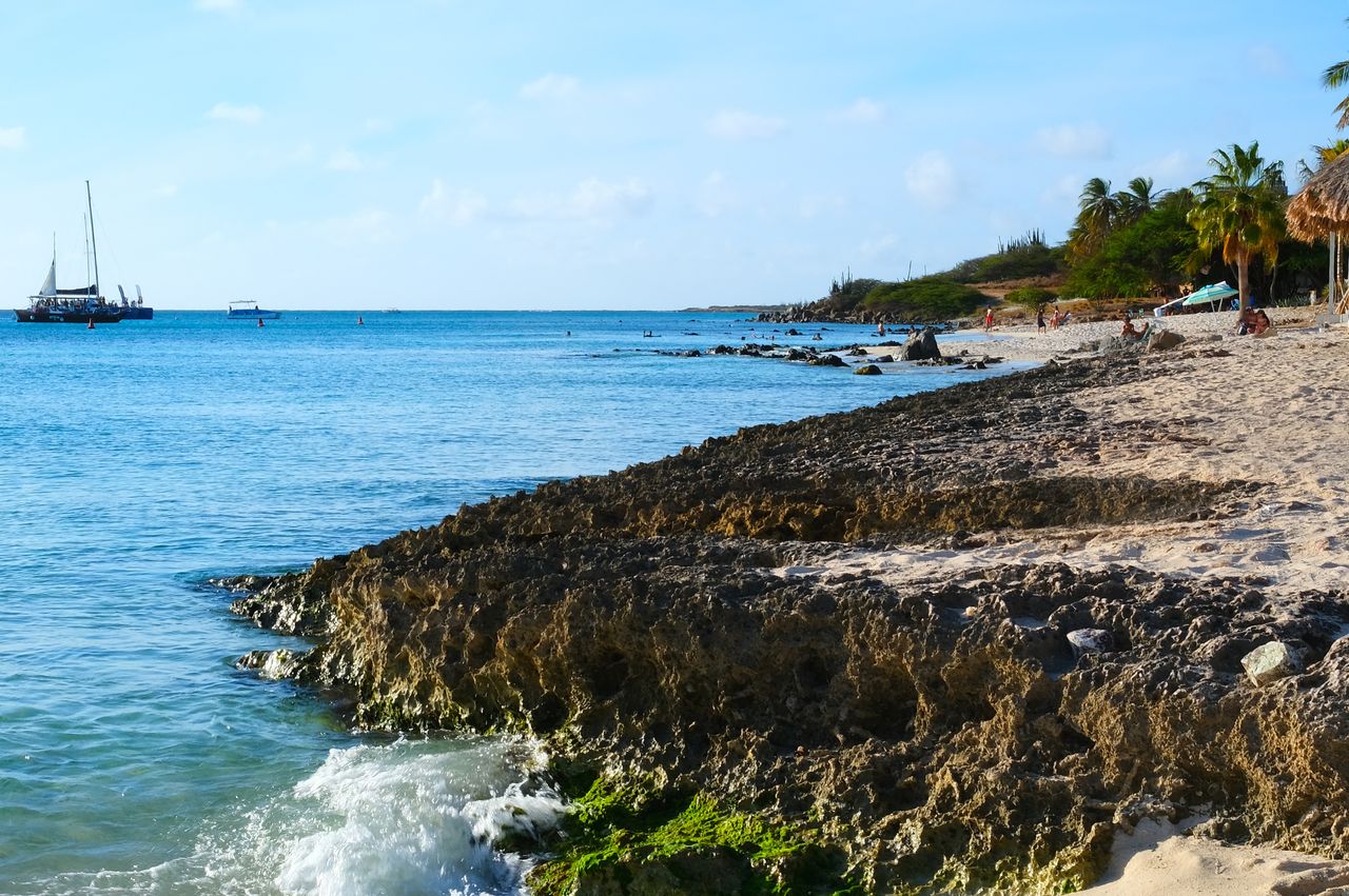 Coastal view of Aruba showing rocky shoreline calm ocean and sailboats in the distance