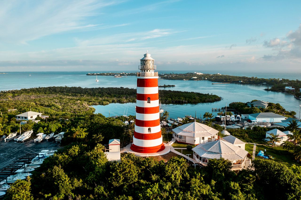 A red and white striped lighthouse near the water surrounded by greenery and buildings