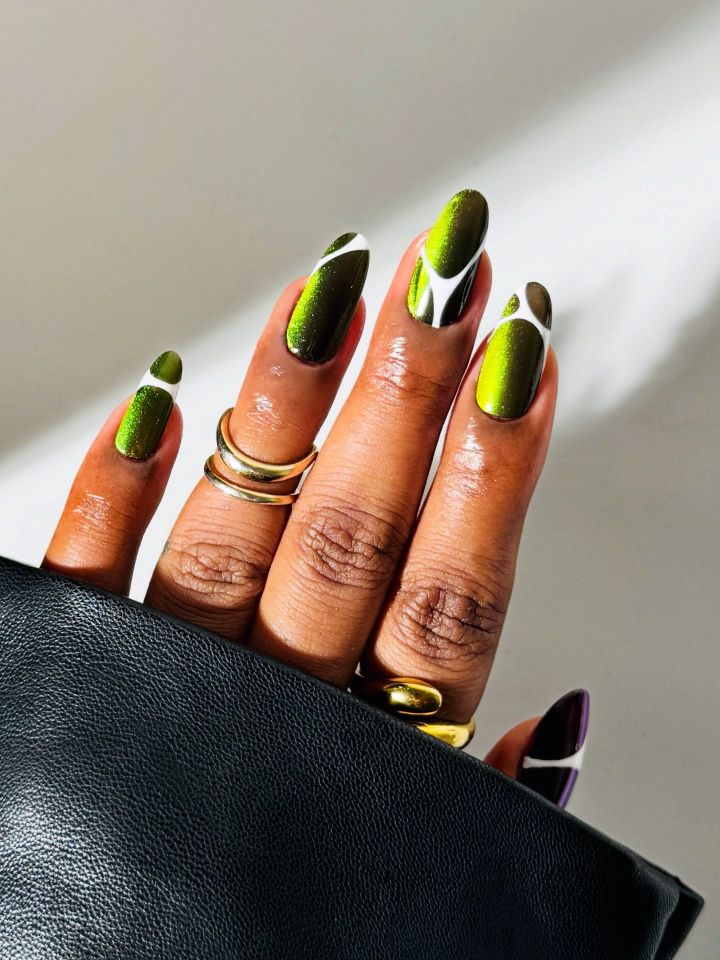 A hand with intricate nail art involving green and white designs adorned with gold rings against a light background