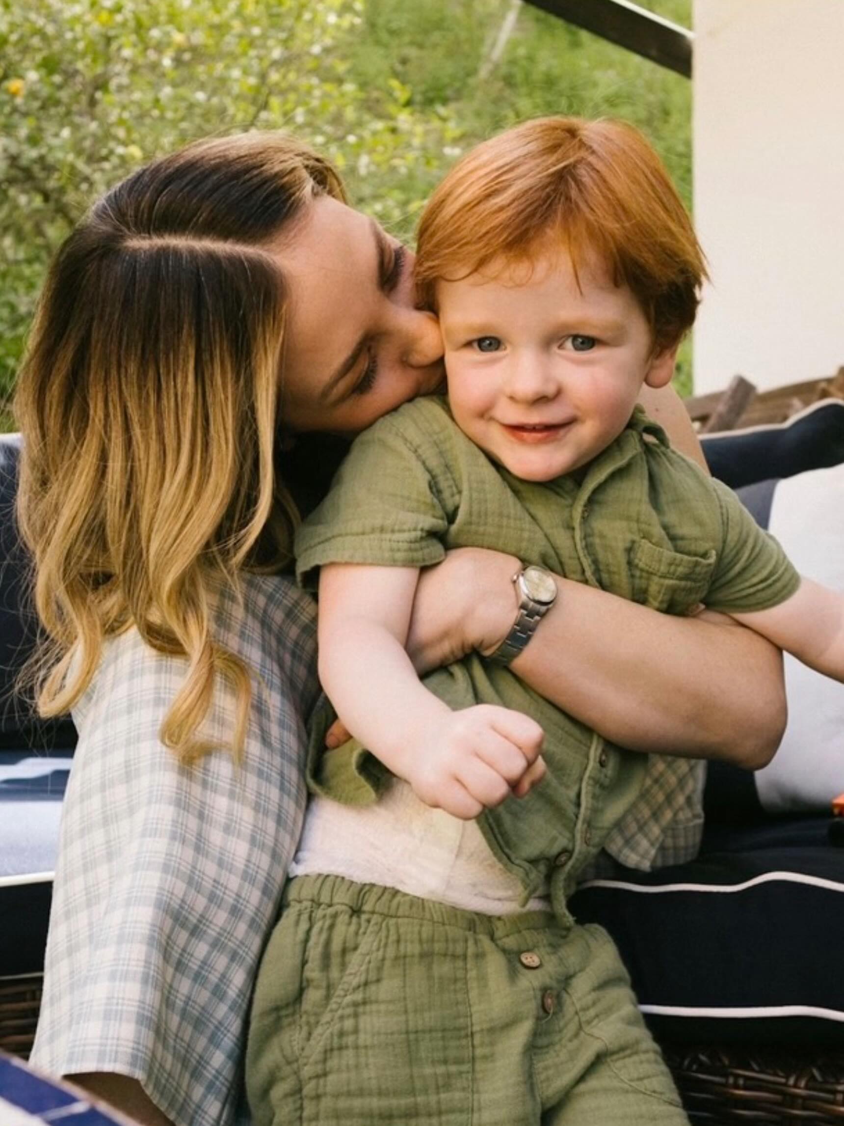 A woman kissing a red-headed child on the cheek.