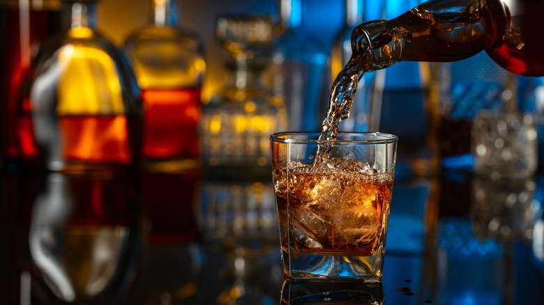 Close-up of pouring whiskey into a glass over ice
