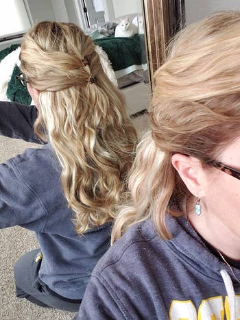 Person with styled half-updo curls, wearing a casual sweatshirt. Mirror reflection shows the hairstyle's back view