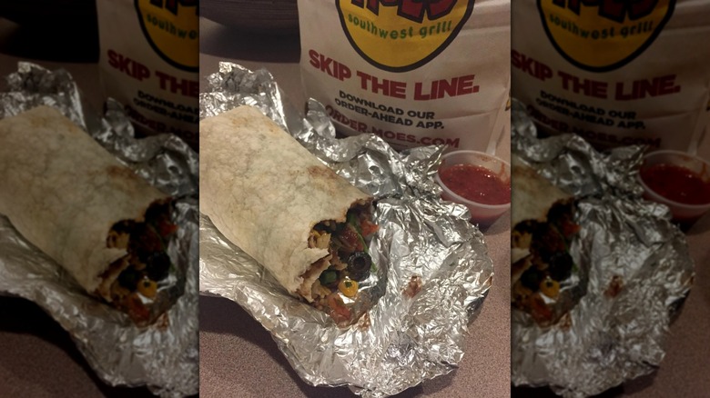 Half eaten burrito on foil in front of Moe's takeout bag, mirrored image
