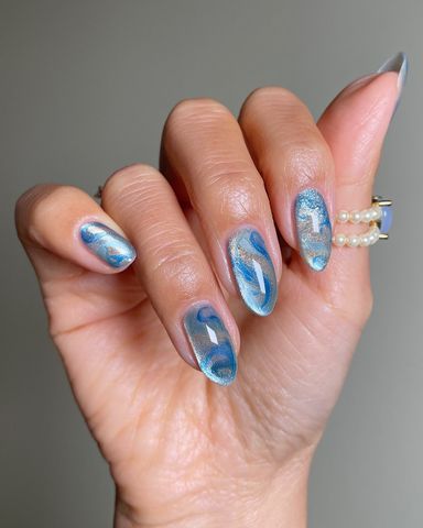 A hand with nails painted in an artistic design adorned with a wave pattern and holding a ring with pearls