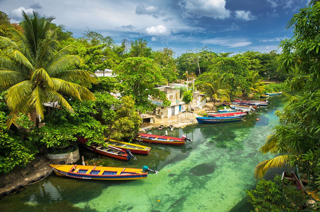 Tropical river scene with moored boats surrounded by lush vegetation and small houses