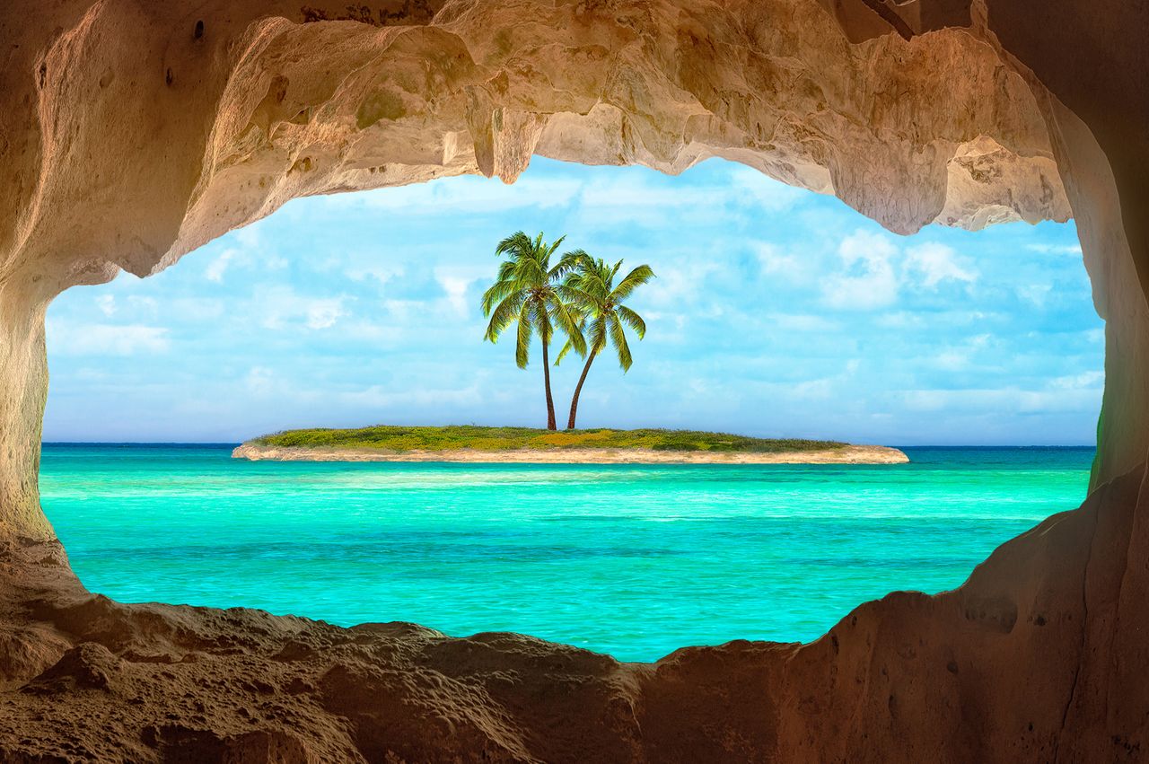 View from a cave of an island with two palm trees surrounded by water