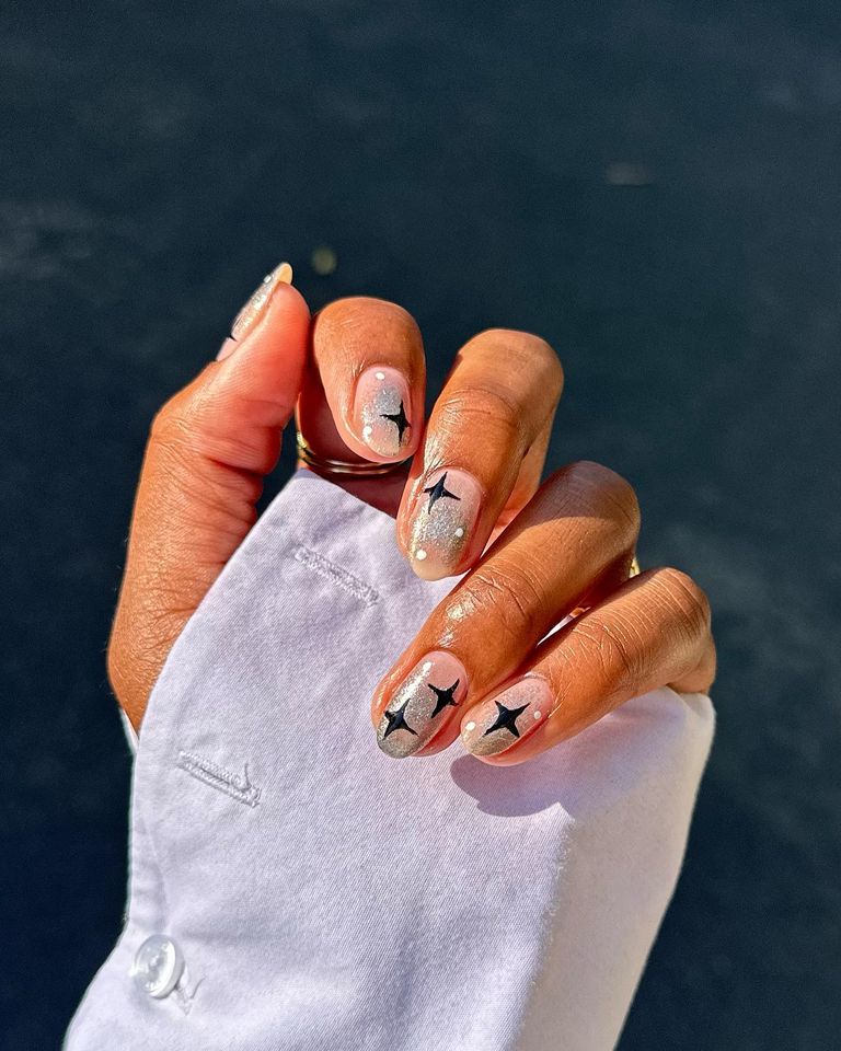 A hand displaying nail art featuring star designs on clearglossed nails