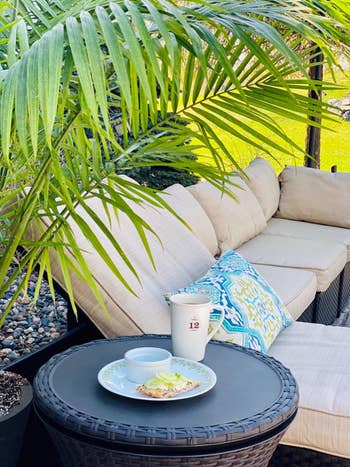 Outdoor patio with wicker lounge, tropical plants, and a side table holding a snack and drink, suggesting a relaxing space to unwind