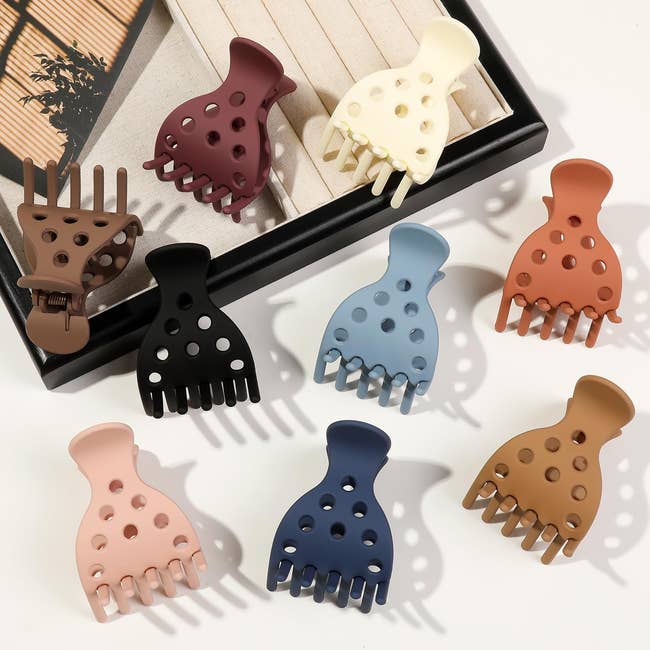 Eight hair claw clips in various designs are displayed on a table, showcasing modern styling accessories