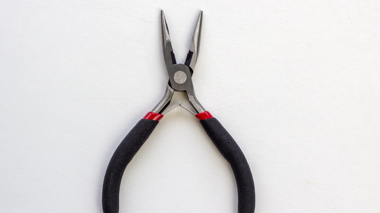 A pair of mini pliers with a black and red handle on a white background
