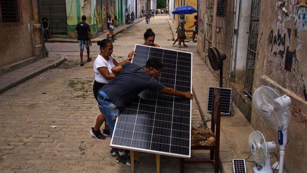 Residents handle a large solar panel on a Havana street, with electric fans nearby, amid Cuba's ongoing power crisis