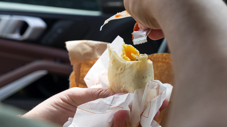 Hand applying sauce to breakfast burrito in car, close up