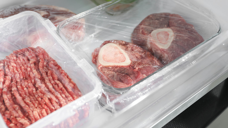 Containers of frozen beef wrapped in cellophane in a fridge