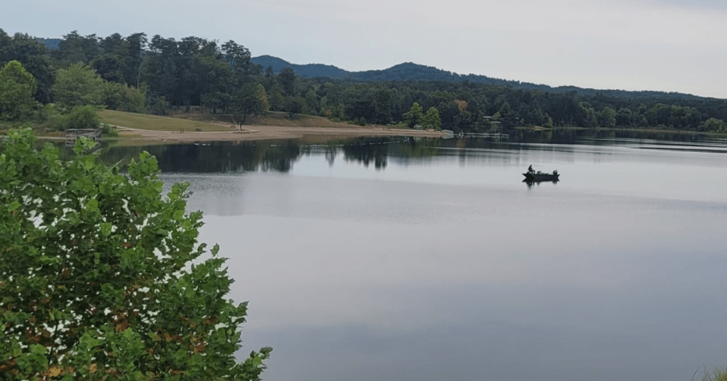 Fishing boat on Deam Lake, Indiana with a tree-lined shore and distant hills in the background.