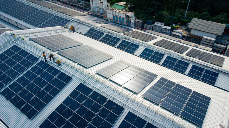 Workers installing rows of solar panels across a large commercial rooftop.