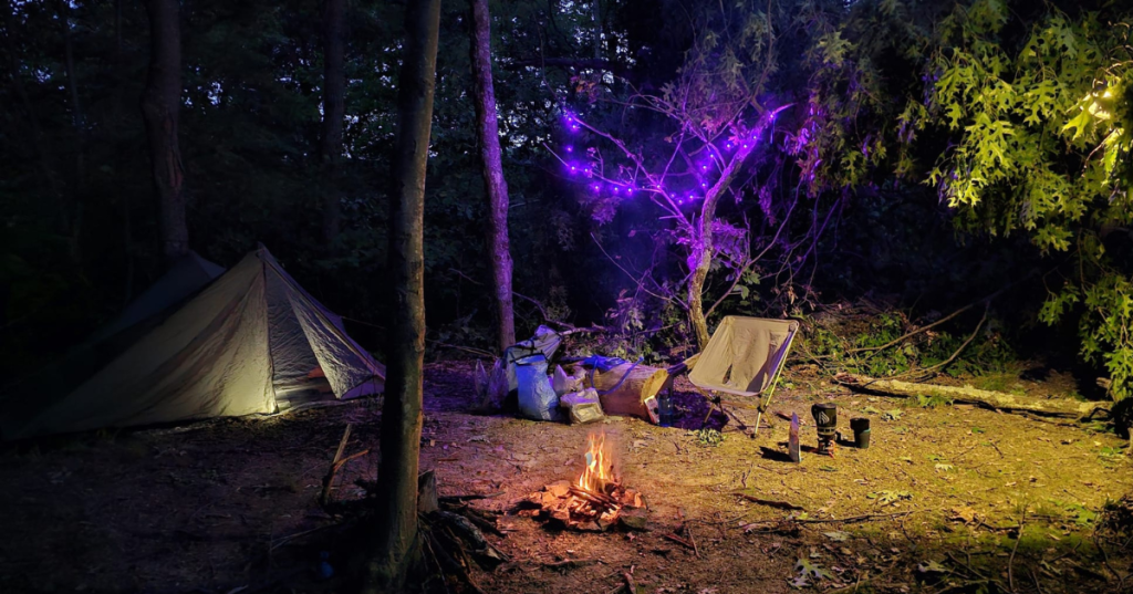 Campsite near Deam Lake, Indiana with a glowing tent, campfire, and purple fairy lights in the trees.