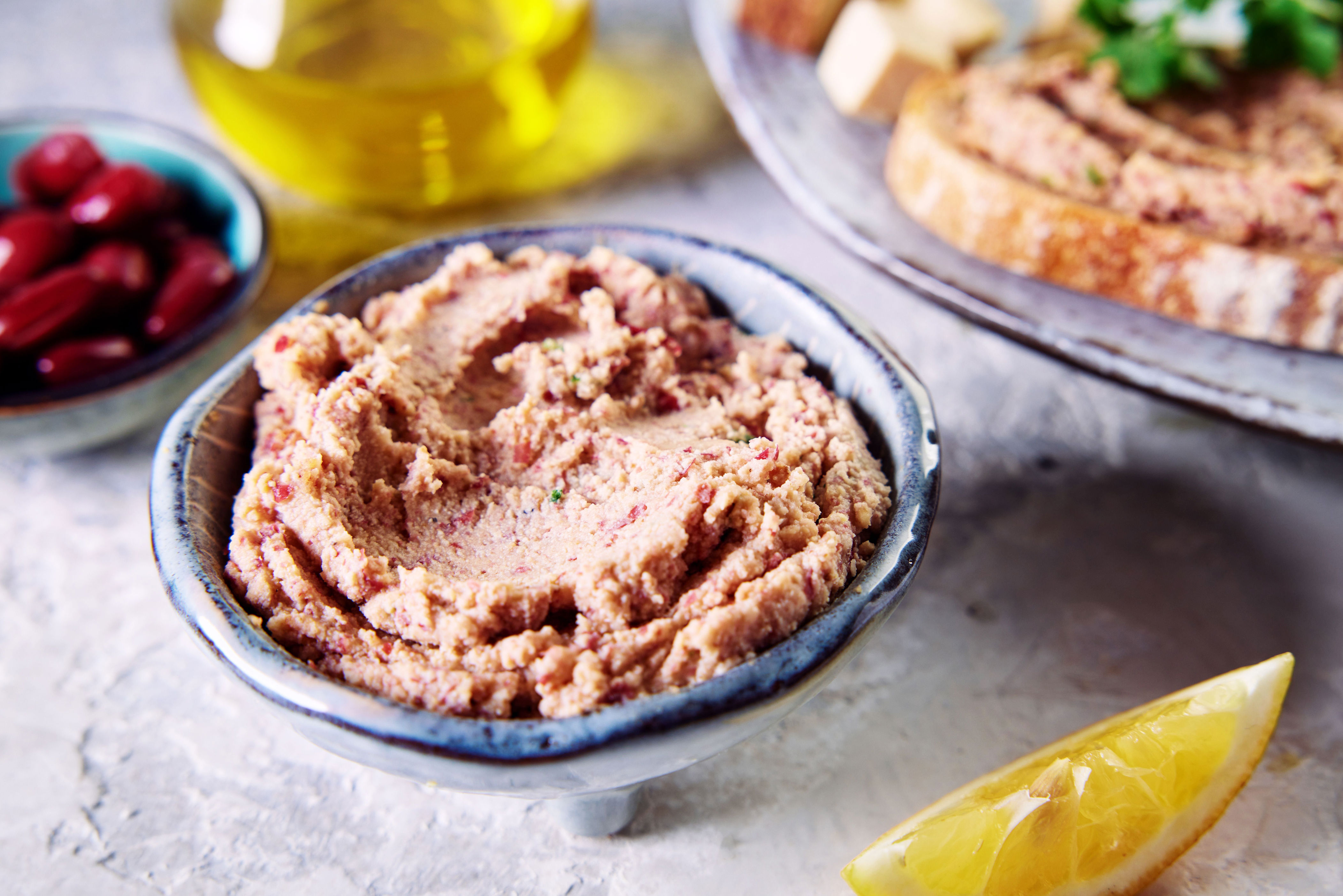 A bowl of bean dip next to a lemon slice, olive oil, and bread spread with dip on a plate