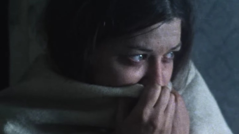 An extra in Threads pulls a blanket around her face, her tear-filled eyes visible over the top
