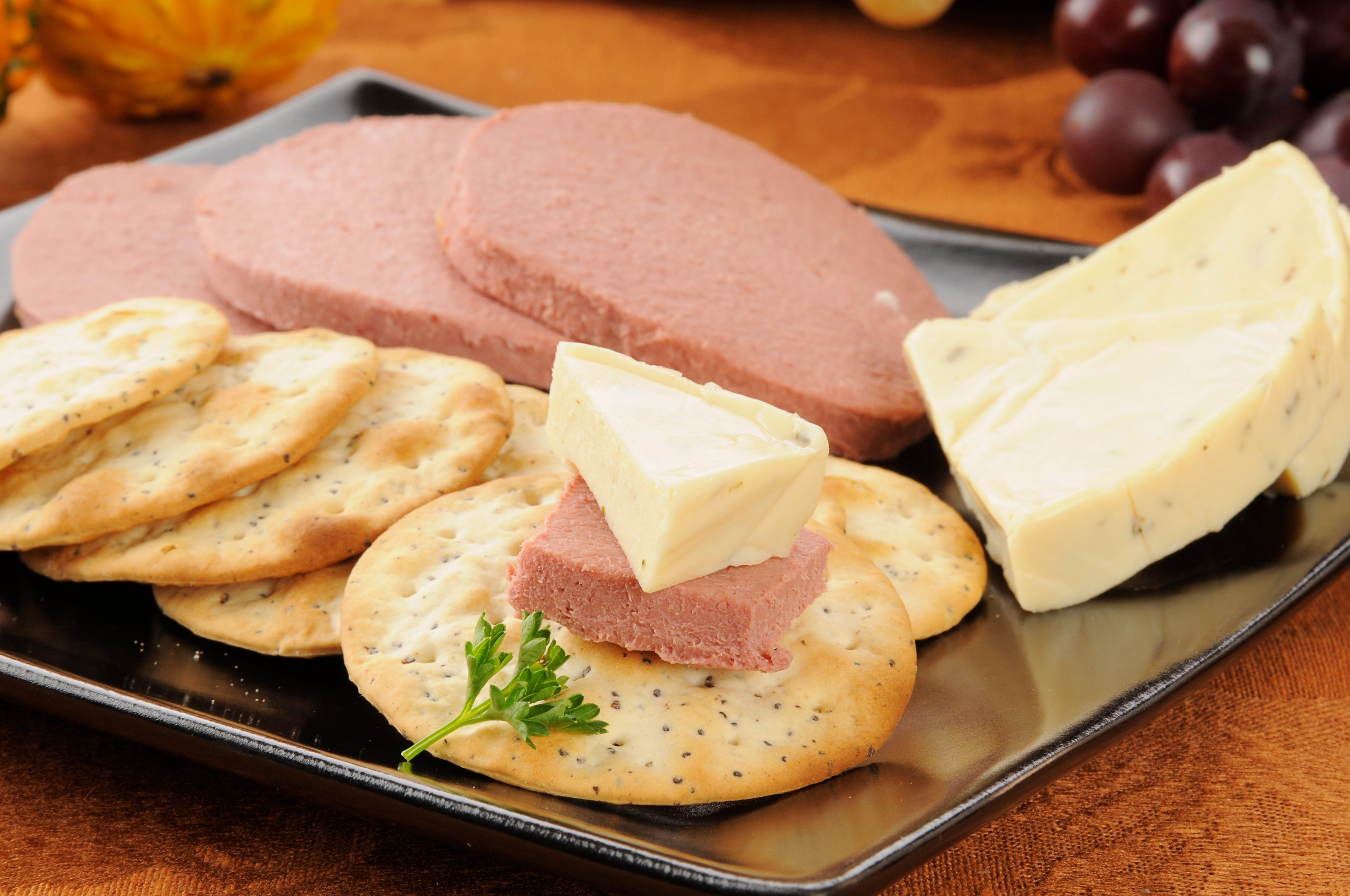 Crackers topped with liver pâté and cheese on a platter, garnished with a sprig of parsley