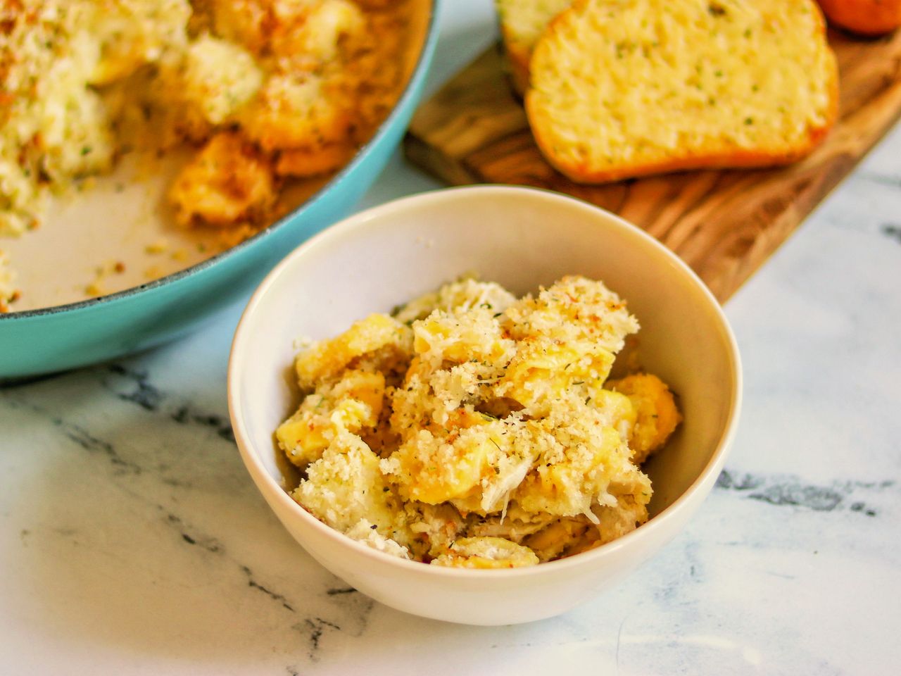 Bowl of tortellini pasta with garlic bread in the background