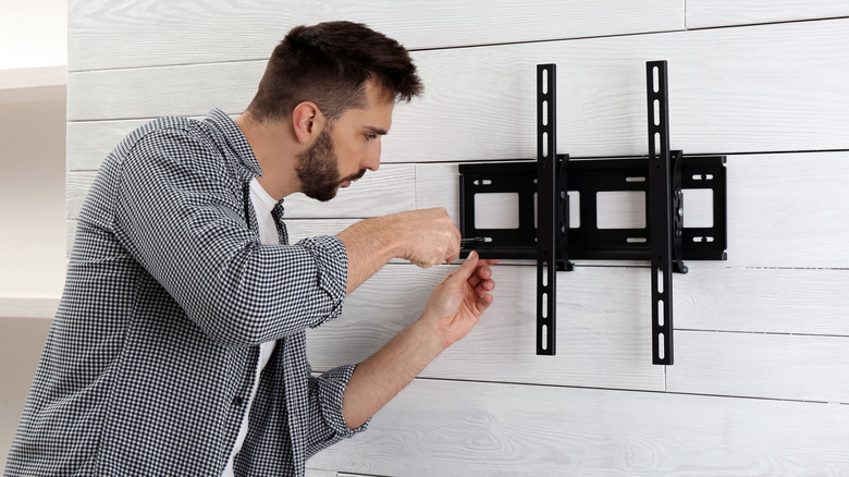 Man with screwdriver installing TV bracket on wall indoors