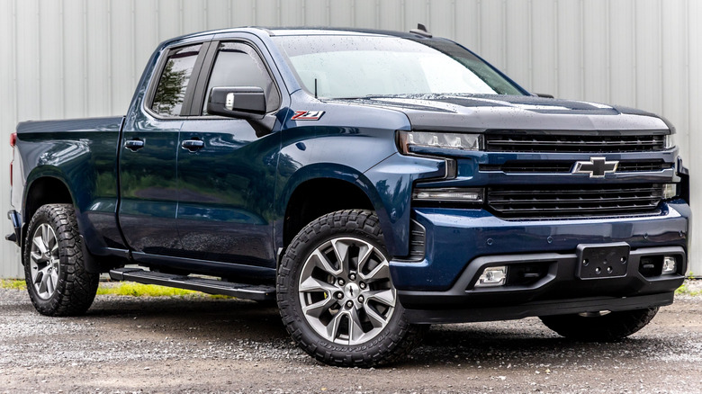 A metallic, dark blue 2023 Chevrolet Silverado parked on gravel.