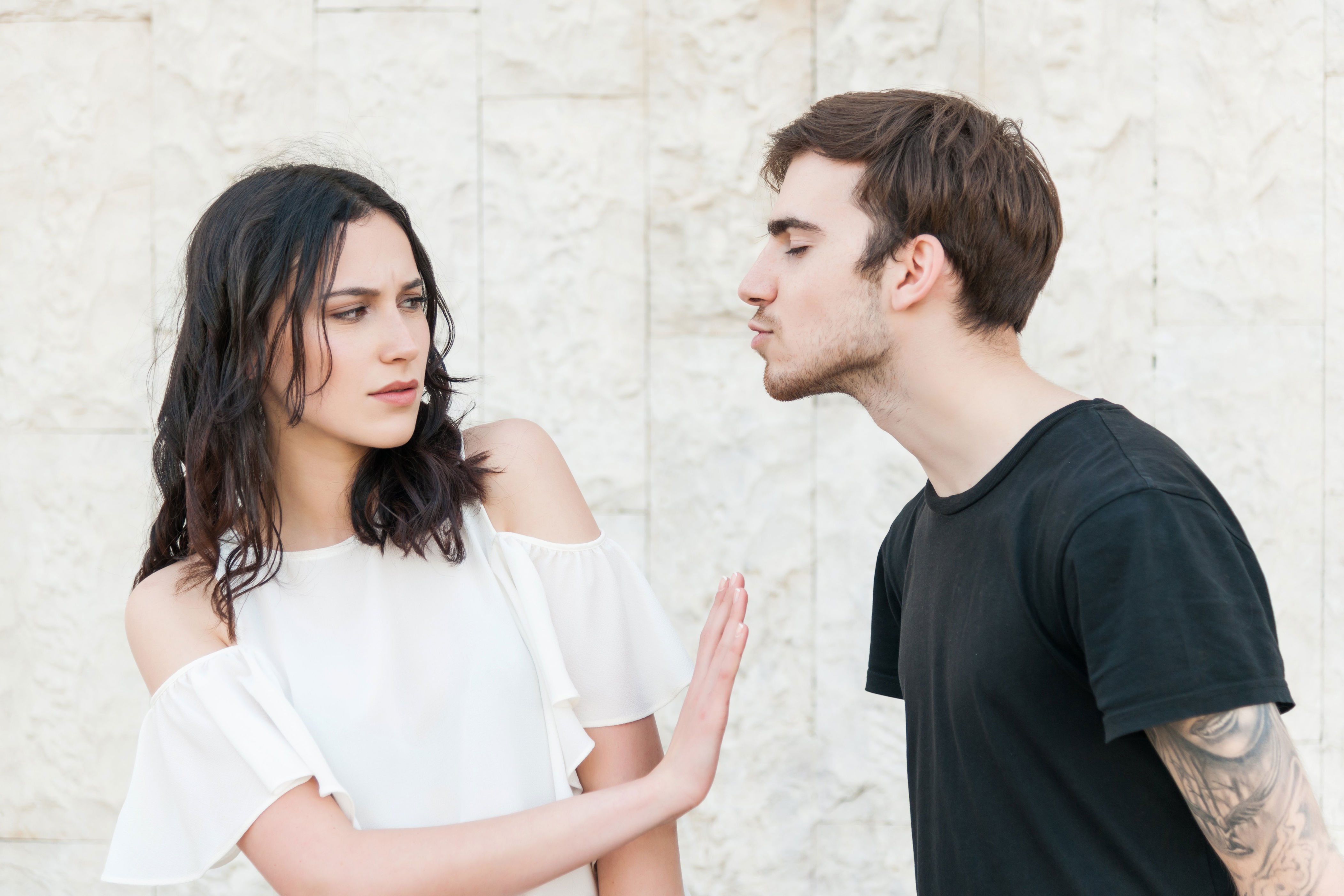 Woman in a white off-shoulder top pushes away a man in a black T-shirt leaning in, suggesting rejection or discomfort in the interaction