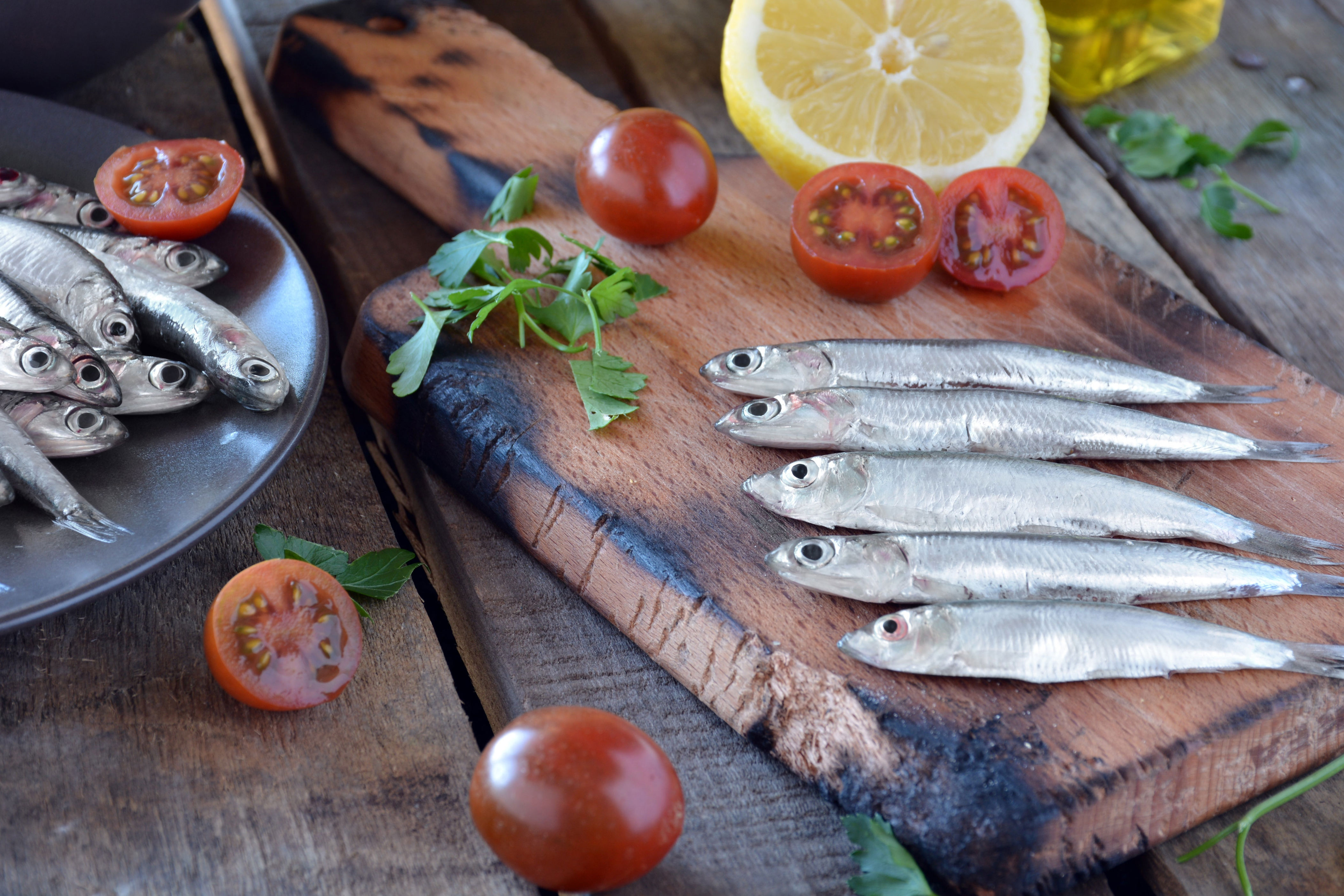 Sardines on a wooden board with cherry tomatoes, parsley, and a lemon slice, ready for preparation