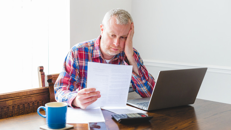 Person rpaying a bill beside a laptop and calculator at a table.