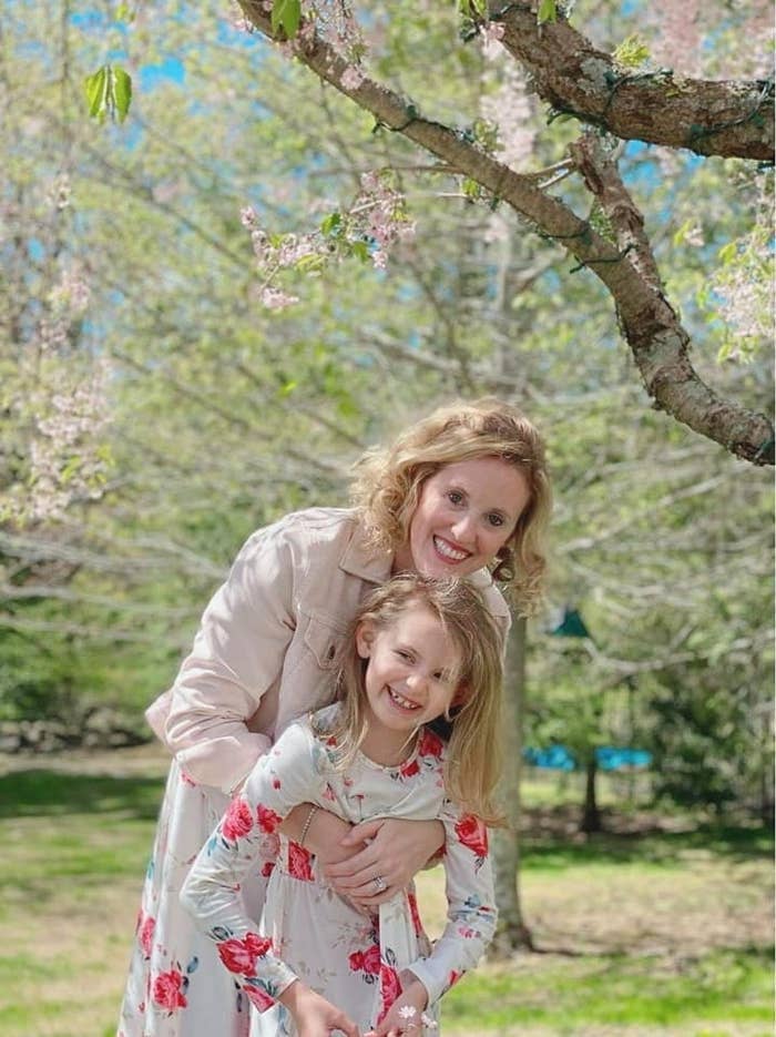 Woman and girl in floral dresses smiling under a blooming tree in a park
