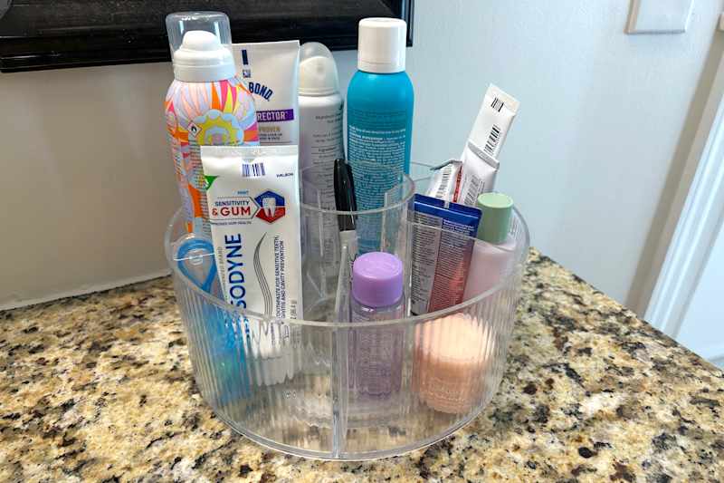Clear organizer filled with various skincare and dental products on a granite countertop.