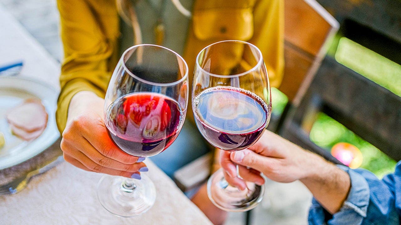 Two people cheers glasses of red wine.