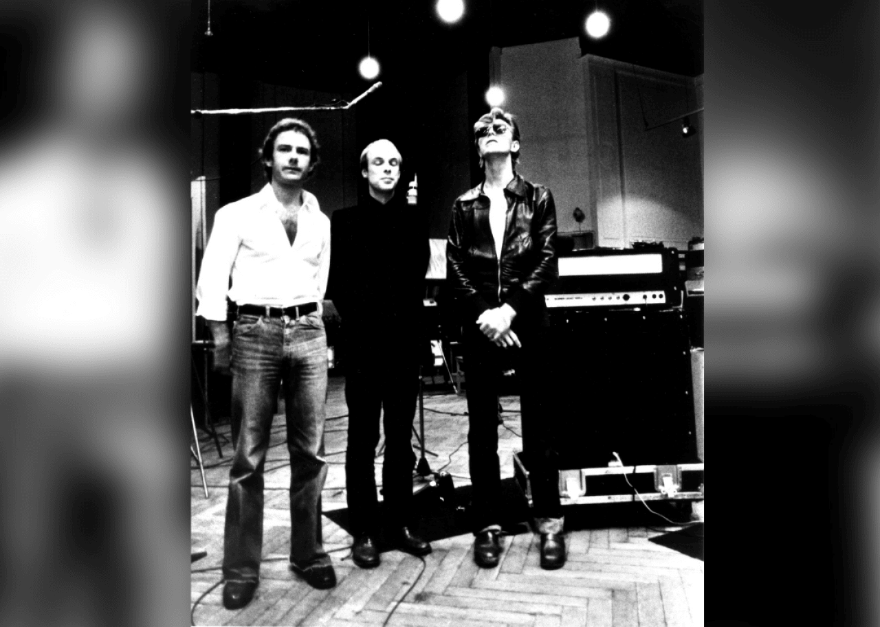 Two men and Bowie stand in a recording studio.