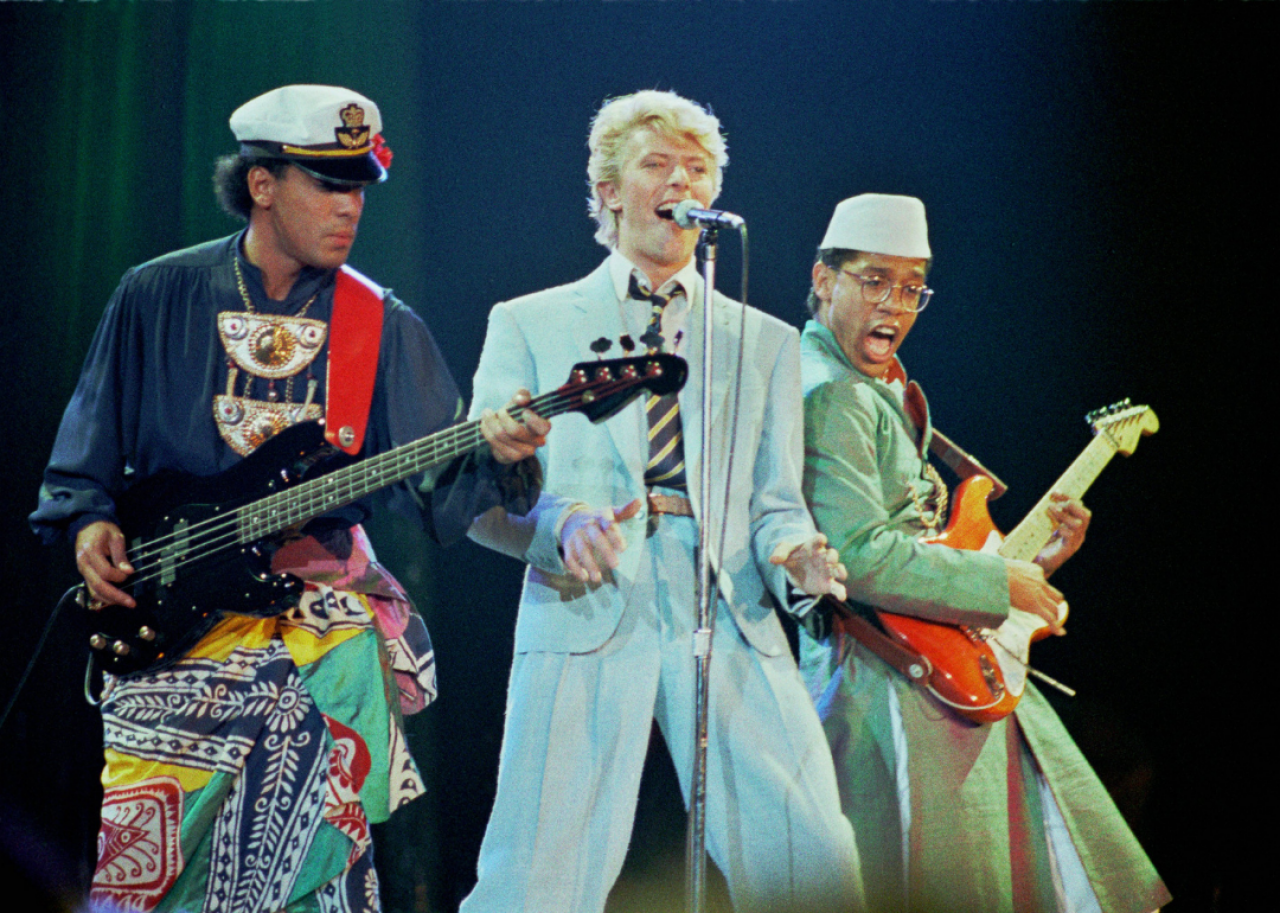 Bowie sings on stage with a bassist and guitarist performing alongside him.