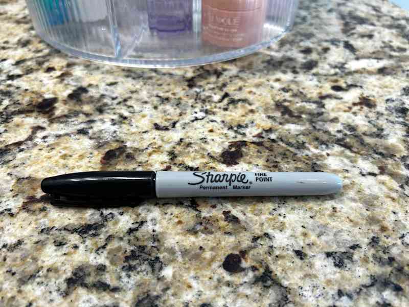 A fine point Sharpie permanent marker resting on a speckled granite countertop, with a clear container in the background.
