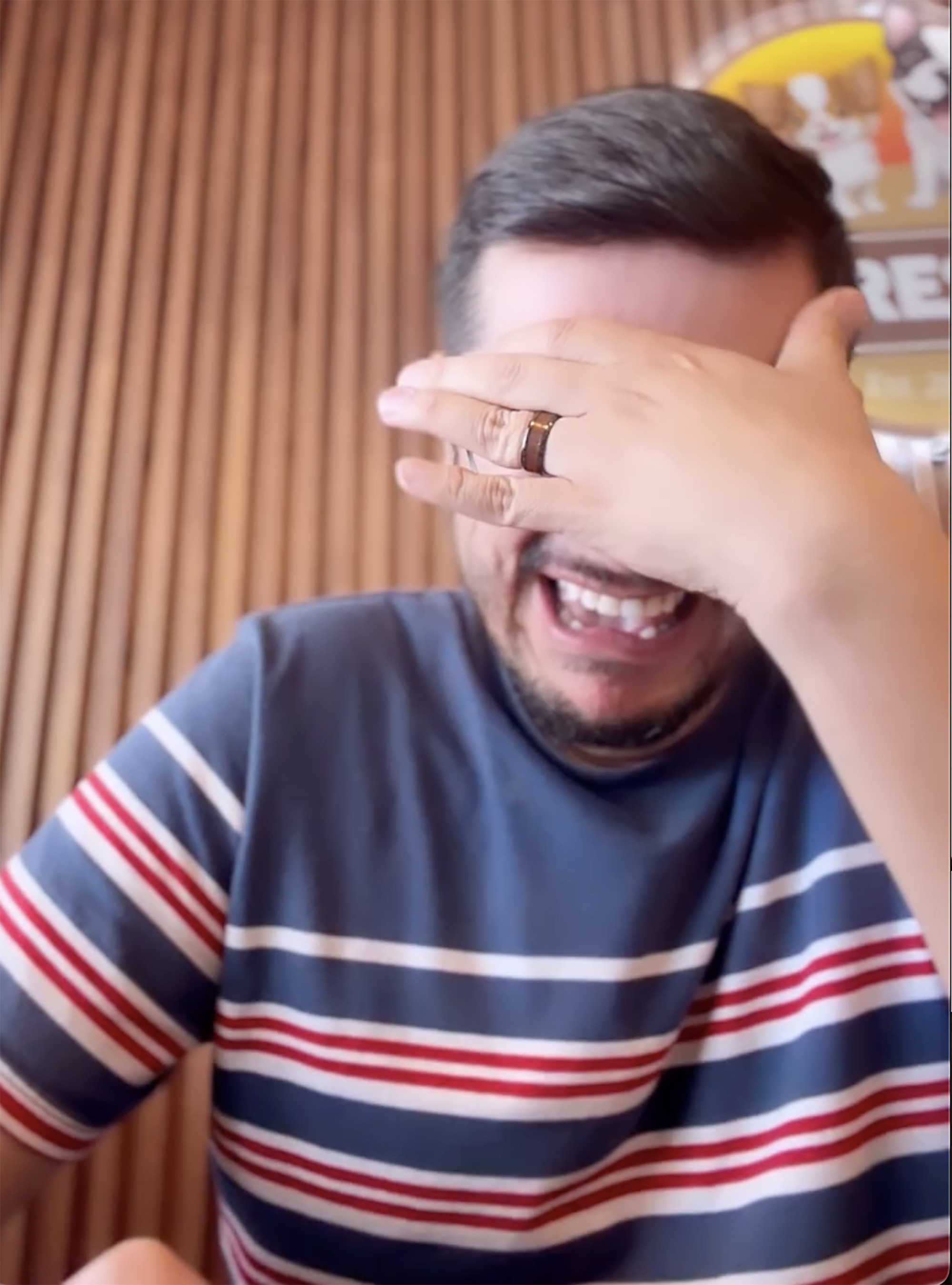 Man in a striped shirt laughing with his hand covering his face.