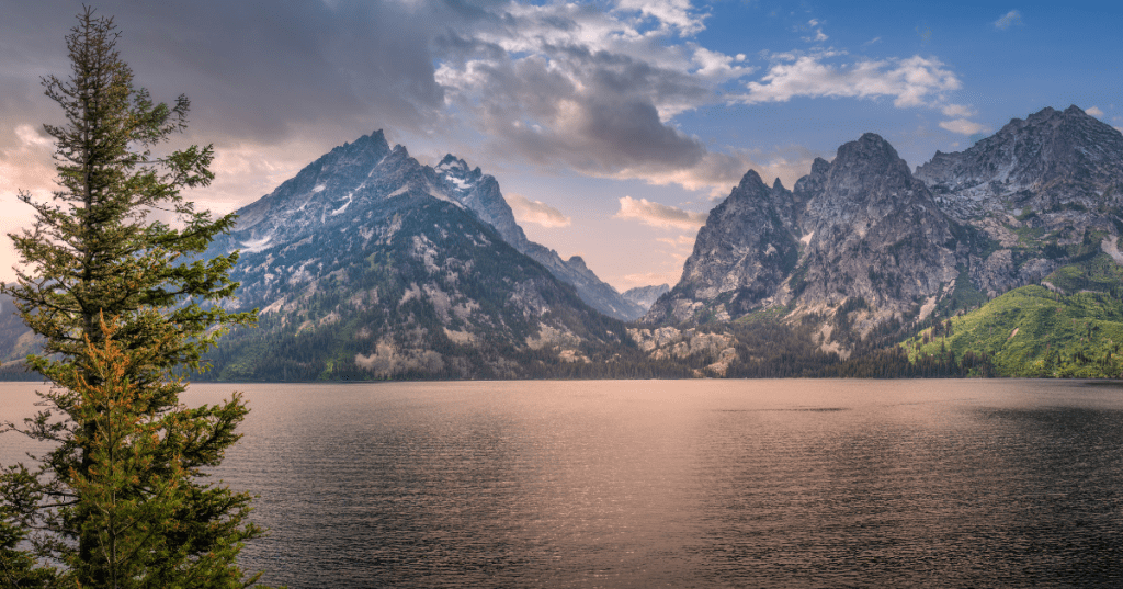 Jenny Lake in Grand Teton National Park reflects a pink sky at dusk. The Teton Mountains loom behind the lake.