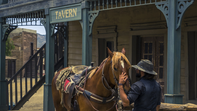 A man and his horse standing in front of an old west tavern.