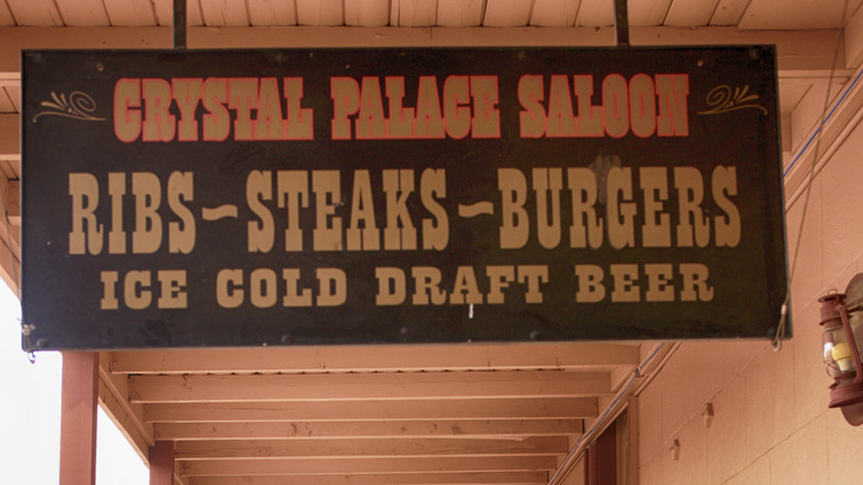 A brown sign for Crystal Palace Saloon, that mentions ribs, steaks, burgers and ice cold beer.