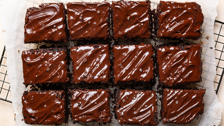 A chocolate frosted sheet cake cut into equal squares according to the grid method, resting on a baking sheet on a wire rack