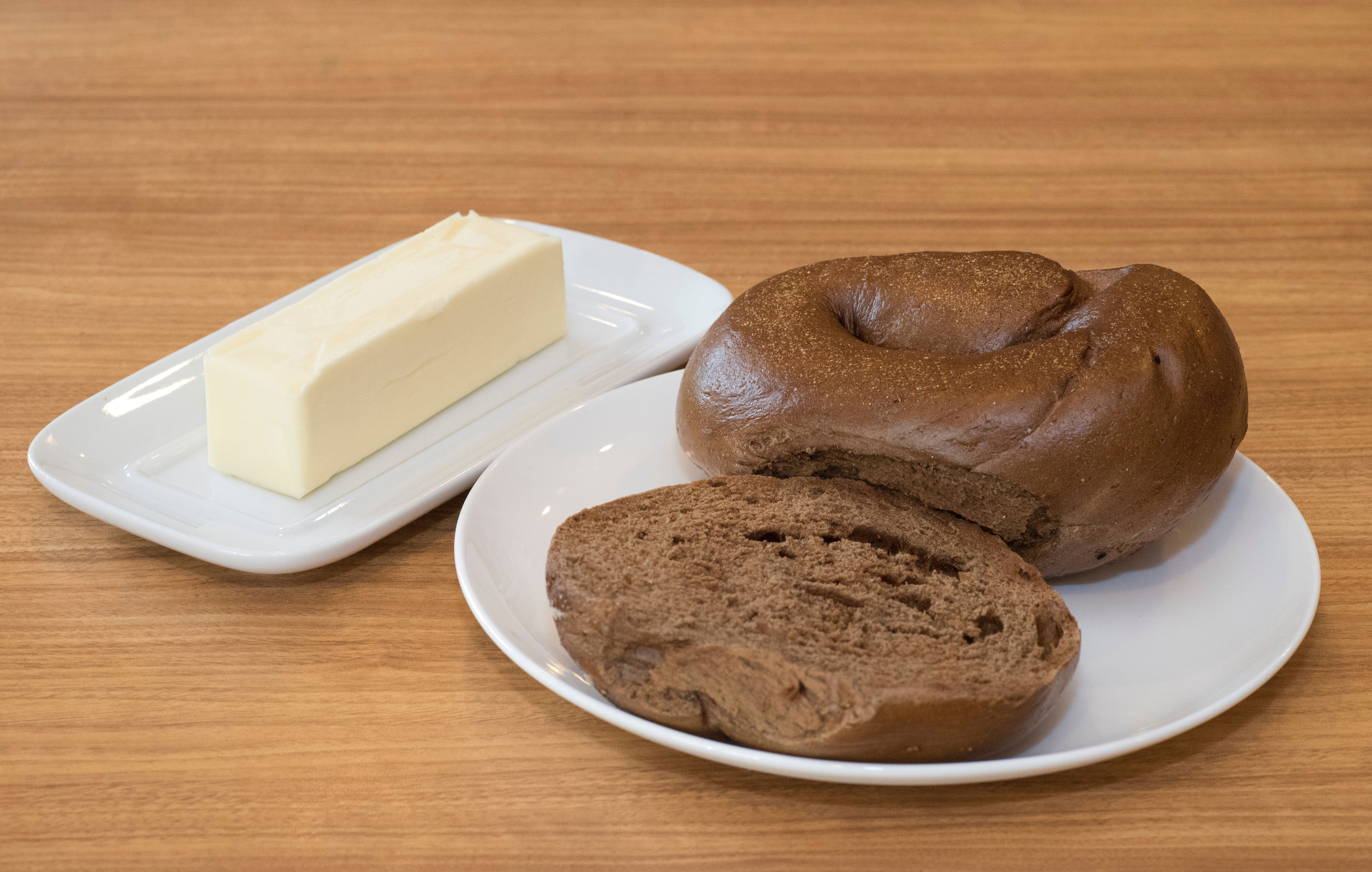 Bagel sliced in half on a white plate next to a rectangular block of butter on a dish, placed on a wooden table