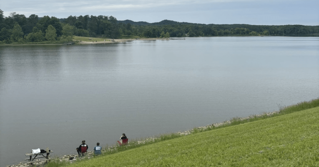 People relaxing in lawn chairs on a grassy hill overlooking Deam Lake in Indiana.