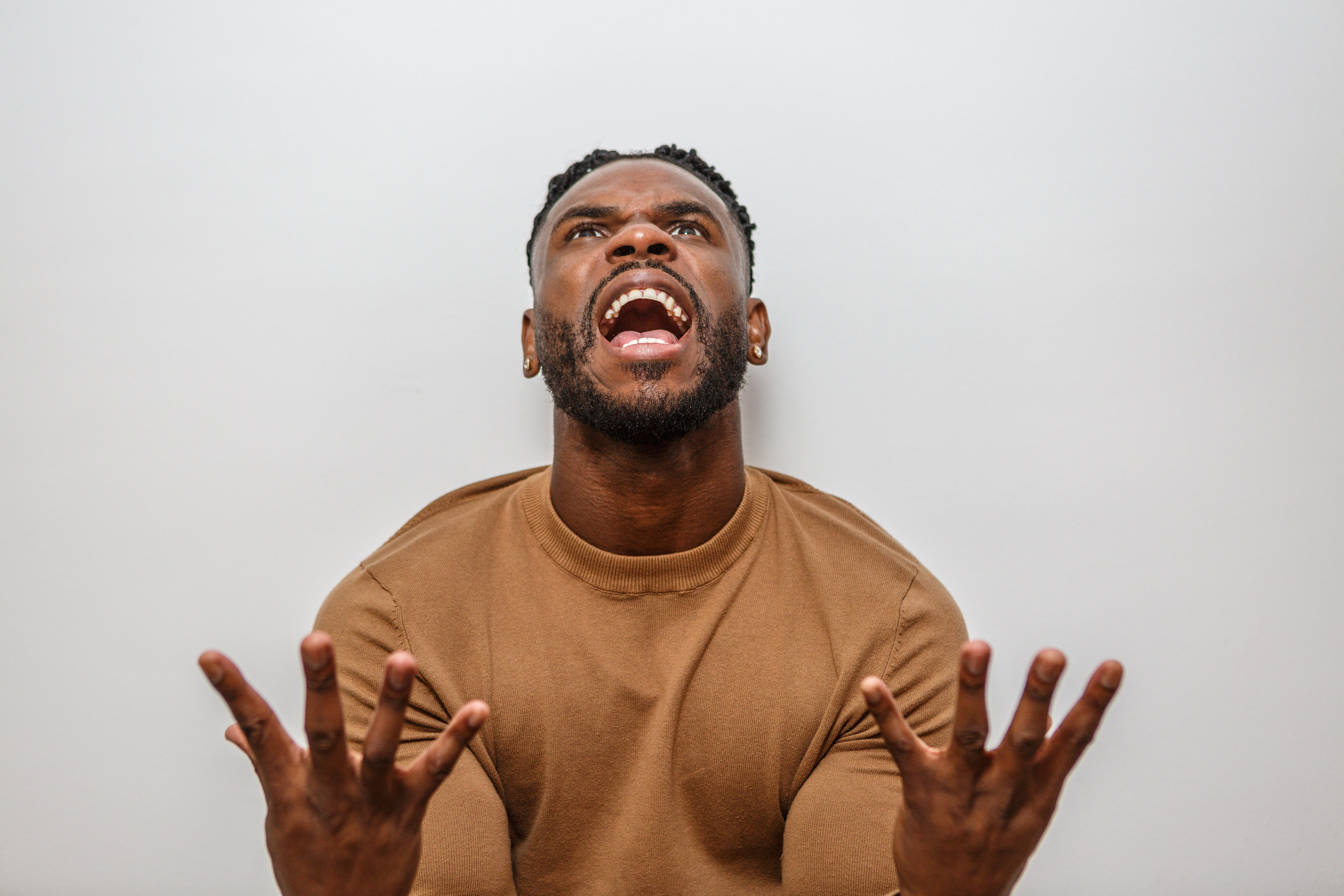 Person looking upward with an expressive, open-mouthed look, hands raised. They are wearing a casual long-sleeve shirt