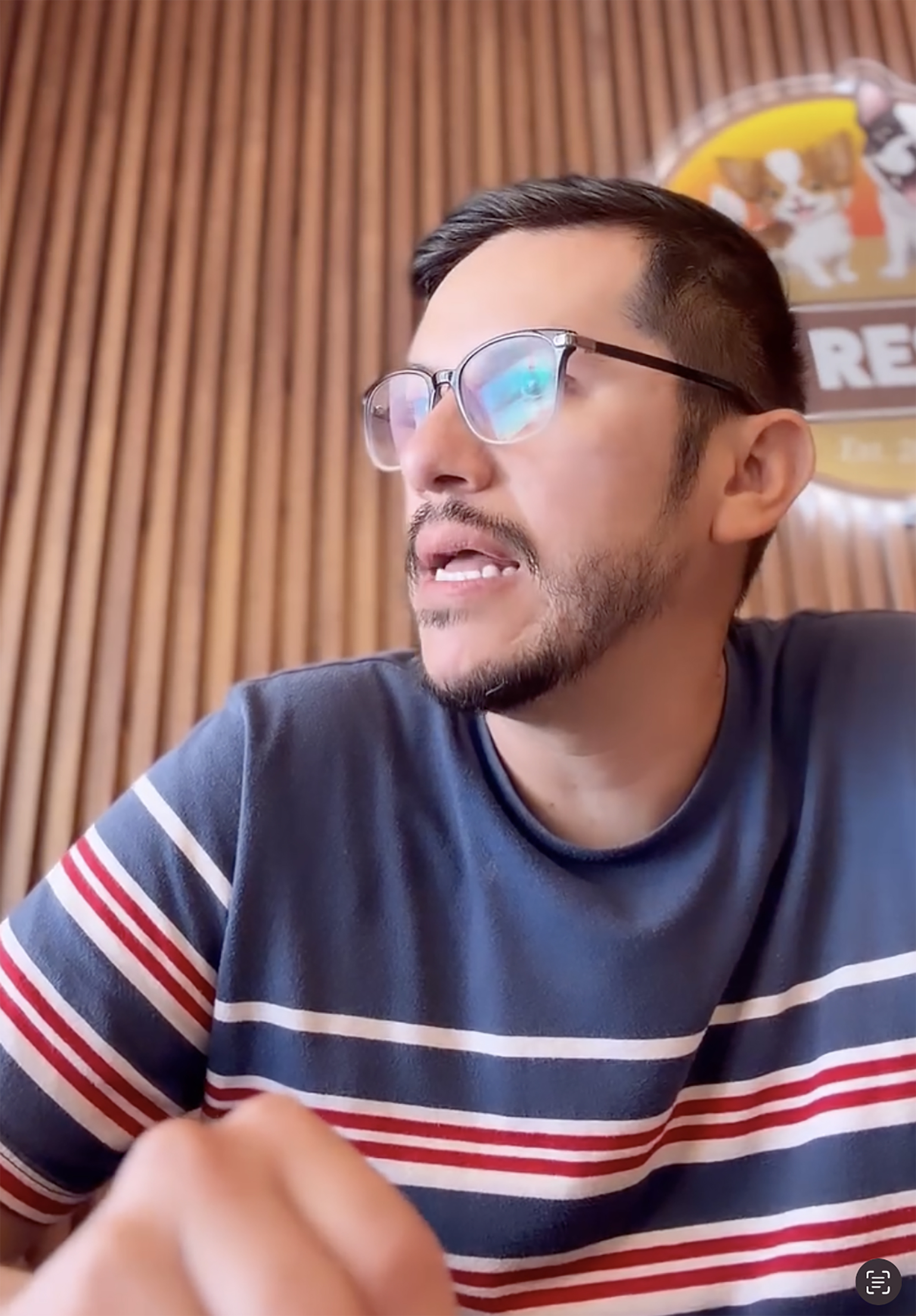 A man with glasses and a beard, wearing a striped shirt, looks to his right while talking.