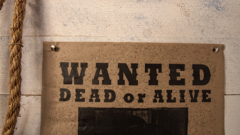 A brown wanted poster that reads wanted dead or alive, secured to a wooden wall with push pins.