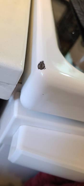 Corner of white kitchen stove before, with a chip out of it, revealing black metal underneath